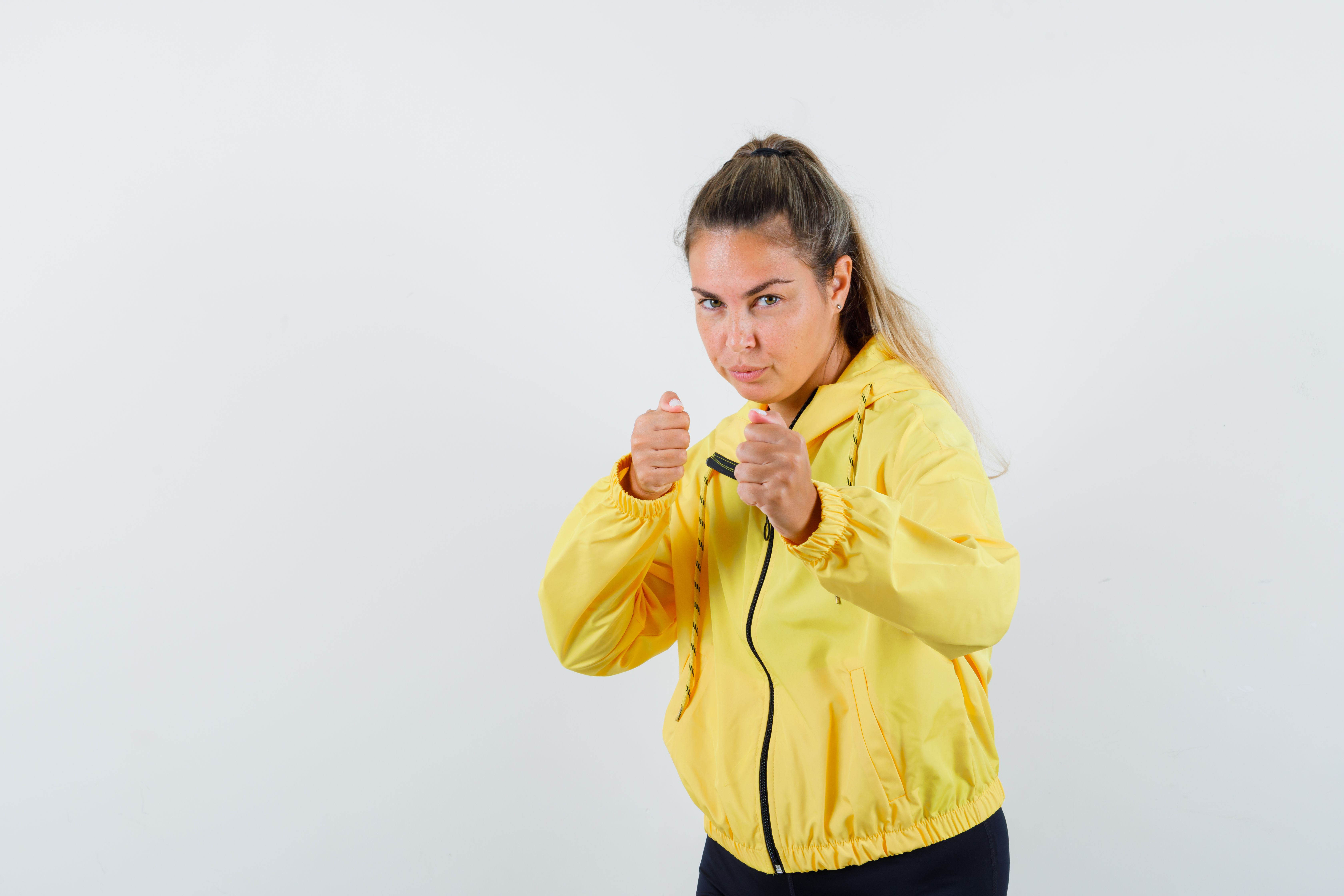young woman standing boxer pose yellow bomber jacket black pants looking cute